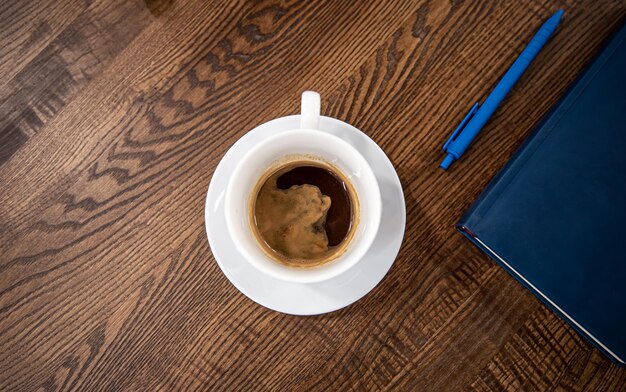 White cup of coffee on a saucer on a wooden table top view