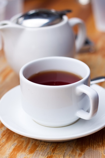 White cup of tea and a pot on wood table