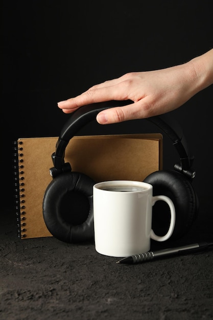 Free Photo a white cup with black headphones and a notebook on a dark background