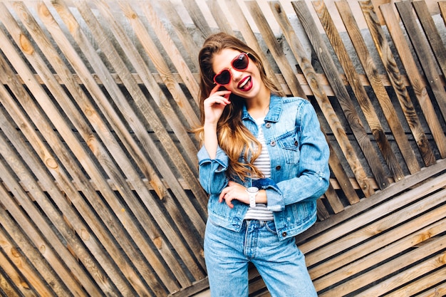 White cute girl in retro style suit laughing and fooling around. Beautiful young smiling woman with long hair  isolated on a wooden fence background.