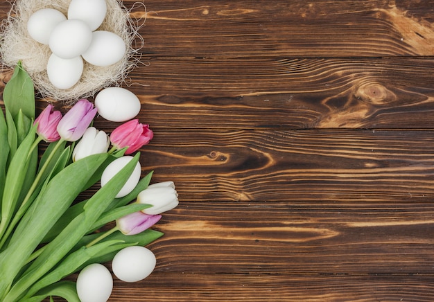 White eggs in nest with bright tulips on wooden table