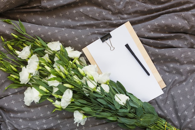 Free photo white eustoma bouquet; clipboard and pen on gray clothes