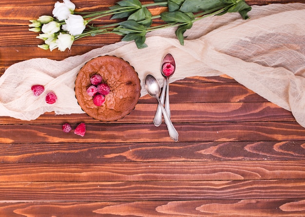 White eustoma flowers; baked caked with raspberry toppings and spoons on cloth over the wooden surface