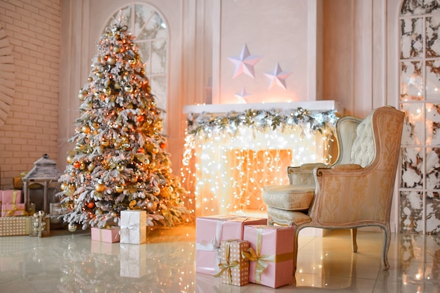 White fireplace decorated with yellow garland and Christmas tree standing by it