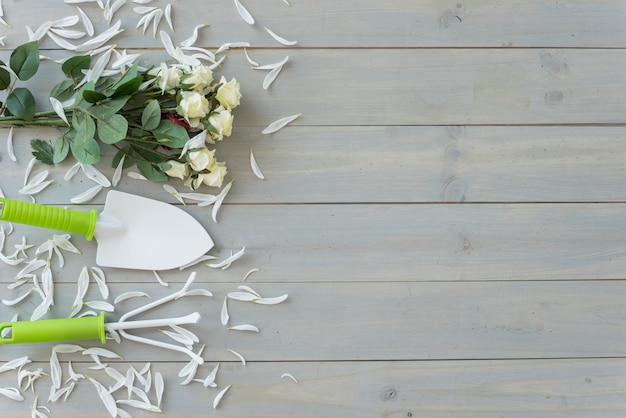 Free photo white flowers, little trowel and rake on grey wooden desk