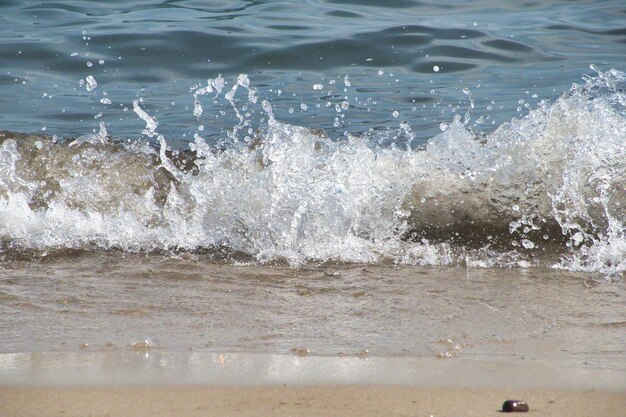 White foam and sea water drop splashes slow motion with sand and blue water