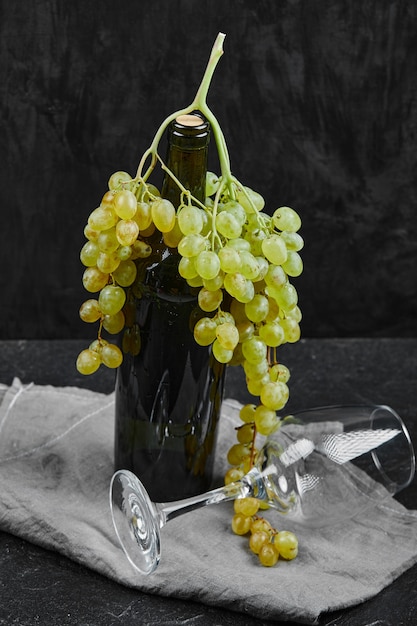 Free Photo white grapes around a bottle of wine and an empty glass on dark background with grey tablecloth. high quality photo