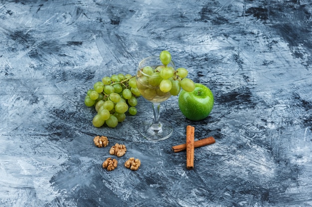 Free photo white grapes, green apple with cinnamon, walnuts, glass of whisky high angle view on a dark blue marble background