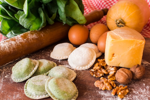 White and green raw ravioli with ingredients in wooden table