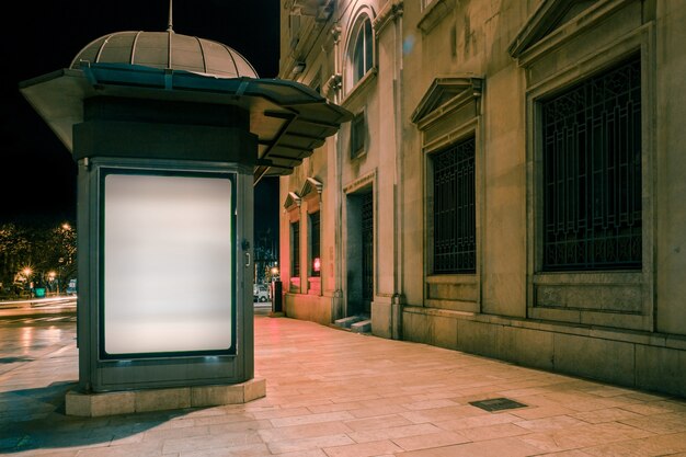 White illuminated blank billboard on footpath at night