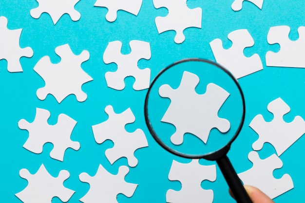 Free photo white jigsaw piece seen through magnifying glass over blue white background