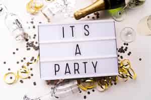 Free photo white light box with it's a party text and champagne bottle over white backdrop