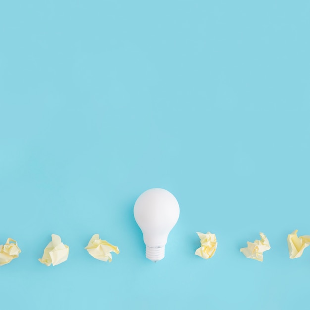 Free photo white light bulb with yellow crumpled paper on colored background