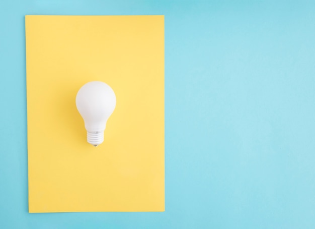 Free photo white light bulb on yellow paper over the blue background