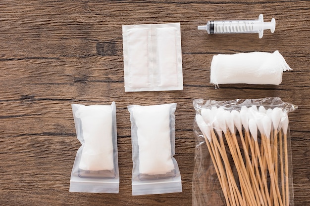 Free photo white medical cotton gauze bandage; syringe and pack of cotton swab on wooden table