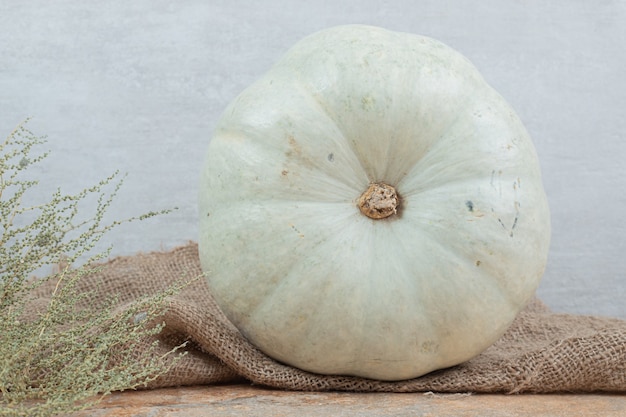 White mini pumpkin on burlap with plant. 