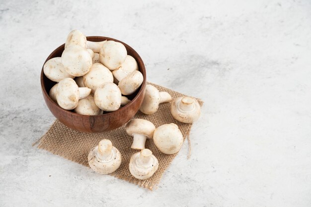 White mushrooms in a wooden cup on a piece of burlap.