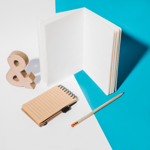 Free Photo white page notebook; spiral notepad; ampersand symbol and pencil on dual background