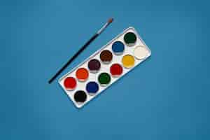 Free photo white palette with twelve various colors being in centre of picture, without con, black brush lying next to paints. phantom blue color. art concept. equipment necessary for painting.