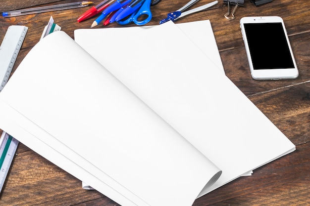 White paper with stationeries and smartphone on wooden table