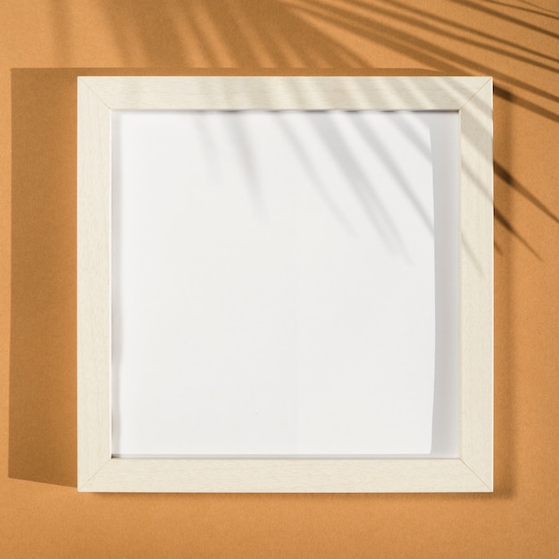 Free photo white photo frame on a beige background with a palm leaf shadow