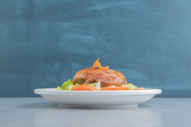 A white plate of chicken fried meat and sliced carrot. 