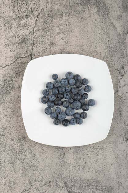 White plate of delicious fresh blueberries on marble surface