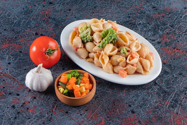 White plate of delicious seashell pasta and fresh salad on marble surface. 