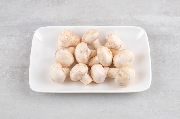 White plate of fresh white mushrooms on stone table. 