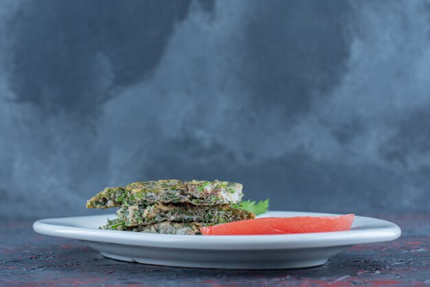 A white plate of fried omelet with herbs and sliced tomato