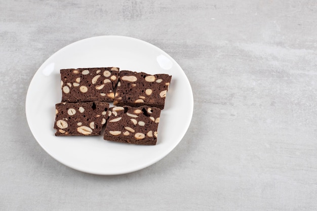 White plate full of brown bread slices with nuts on a stone table. 