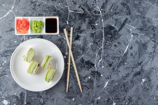 White plate of green dragon sushi rolls on marble background. 