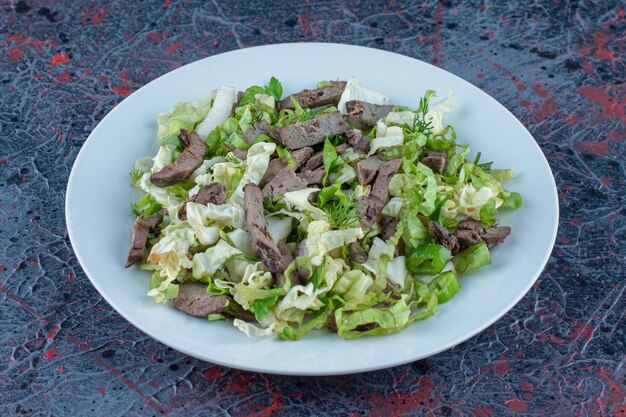 A white plate of meat with vegetable salad. 