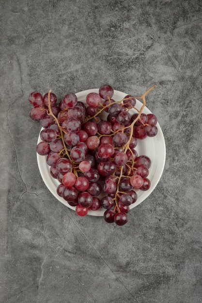 White plate of red delicious grapes on marble table.