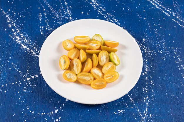 White plate of sliced fresh kumquat fruits on marble surface