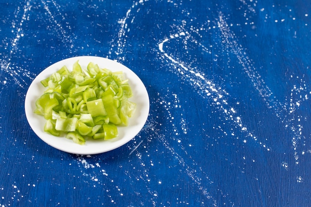 Free photo white plate of sliced green bell peppers on marble surface