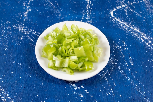 White plate of sliced green bell peppers on marble surface