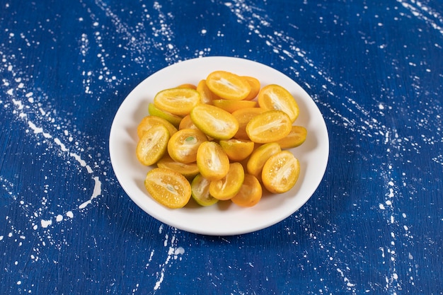 White plate of sliced kumquat fruits on marble surface