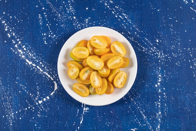 White plate of sliced kumquat fruits on marble table.