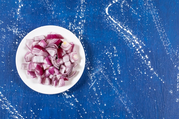 White plate of sliced purple onions on marble surface. 