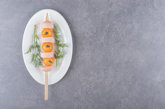 A white plate with boiled sliced sausage with cherry yellow tomato . 