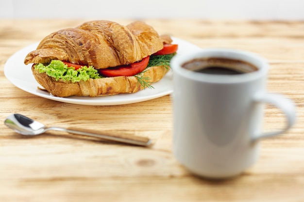 White plate with a sandwich and a coffee cup on a wooden table