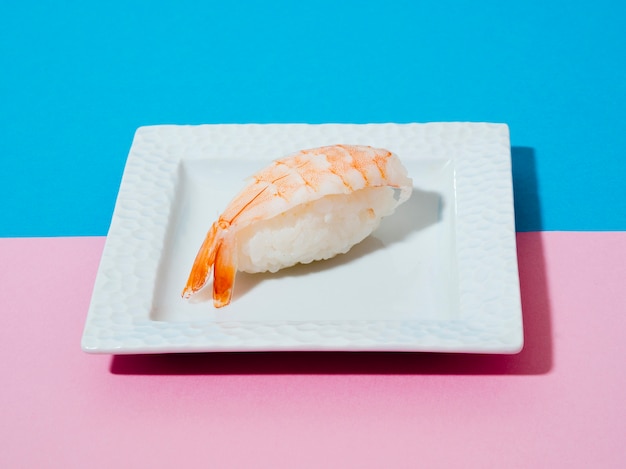 Free Photo white plate with shrimp sushi on a blue and rose background