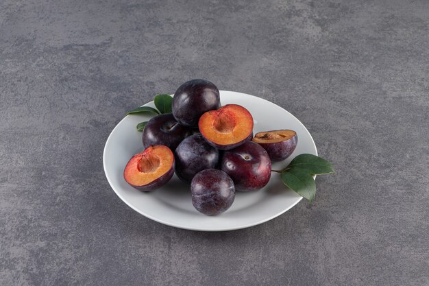 White plate with sliced purple plums on stone background.