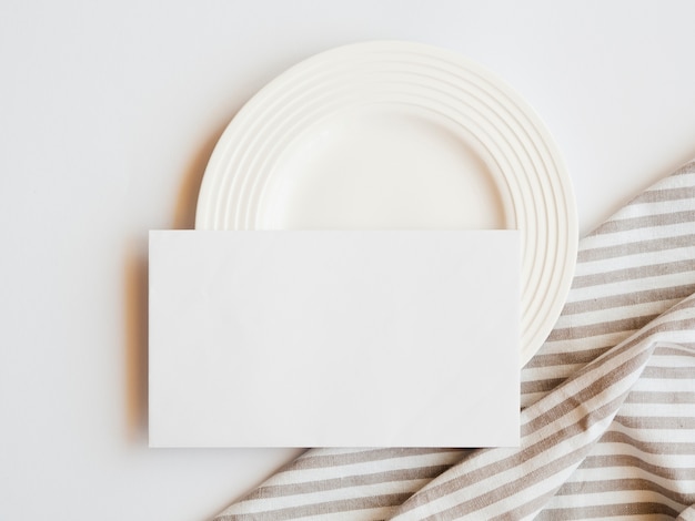 White plate with a white blank and a striped brown and white tablecloth on a white background