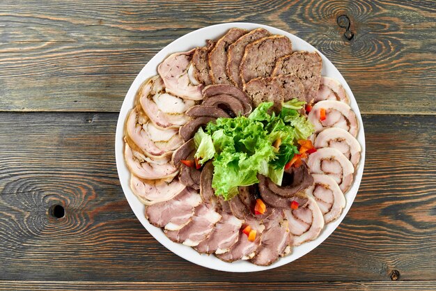 White plate on a wooden table full of stuffed meat slices, decorated with fresh lettuce leaves and paprika pieces.