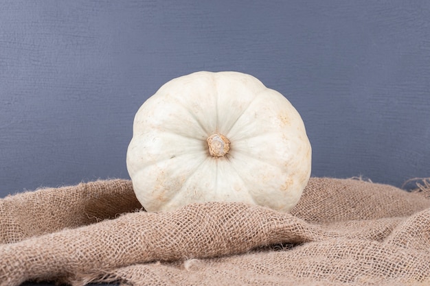 White pumpkin on blue surface with burlap.