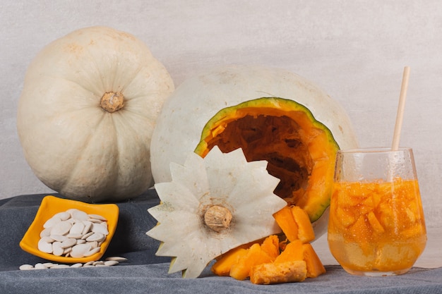 Free Photo white pumpkin, glass of juice and pumpkin seeds on white table.