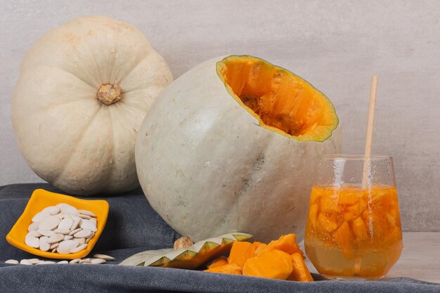 White pumpkin, glass of juice and pumpkin seeds on white table.