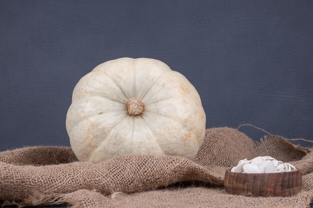 White pumpkin and seeds on blue surface with burlap.